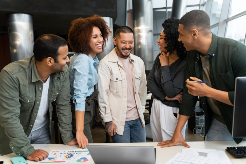 La puissance de l’équipe ! Cinq collègues affichent des sourires radieux et une parfaite harmonie dans un environnement de bureau moderne. L'image capture l'esprit de collaboration et d'efficacité collective au sein de l'équipe.
