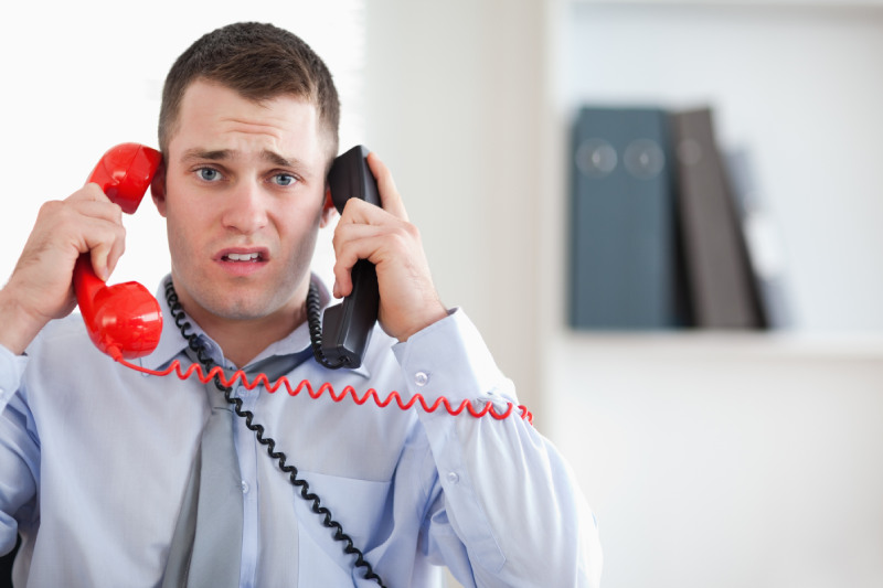 Un commercial anxieux tenant deux téléphones à la main, exprimant une certaine appréhension à l'idée de faire de la prospection téléphonique. Son visage révèle une absence d'enthousiasme et une angoisse palpable. L’image capture les défis et les émotions ressenties par de nombreux professionnels lorsqu'ils sont confrontés à des tâches de prospection téléphonique.