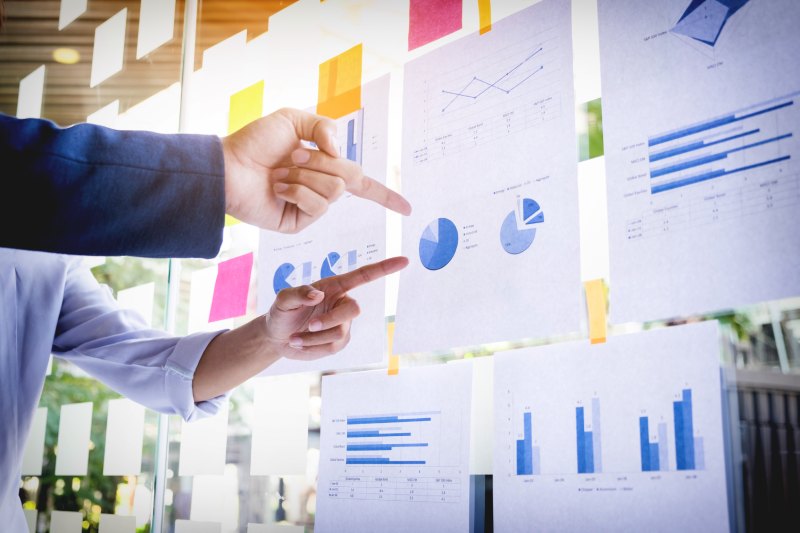 Deux collègues analysant des données et des graphiques sur un tableau vitré dans un bureau moderne et bien éclairé. L’image illustre leur collaboration et l'utilisation des données à jour pour la prise de décisions informées.